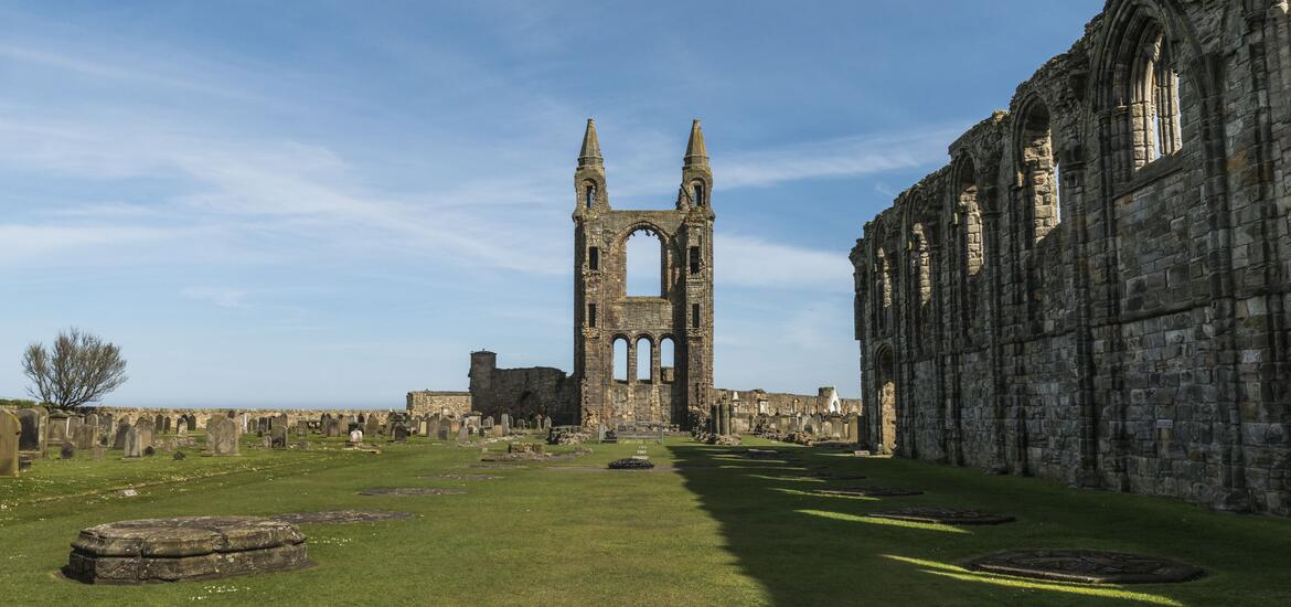 Ruins of St Andrews Cathedral near Fife, with historic stone arches, gravestones, and a blue sky backdrop