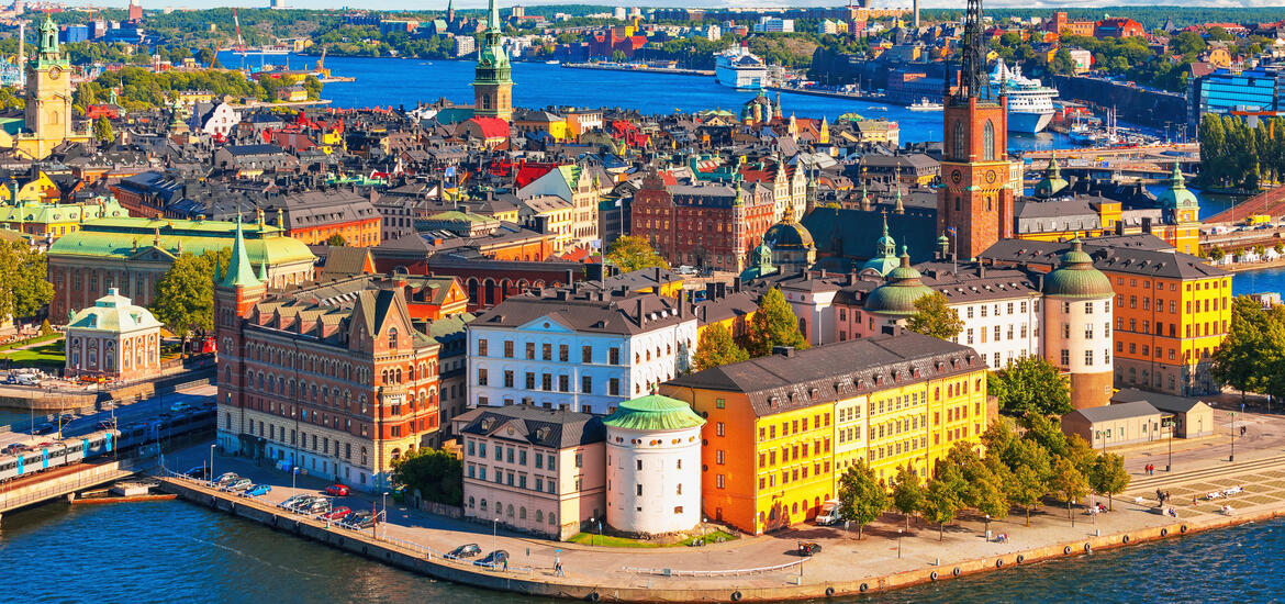 An aerial view of Stockholm’s Old Town, featuring colorful historic buildings, church spires, and the waterfront, with boats and ships visible in the background