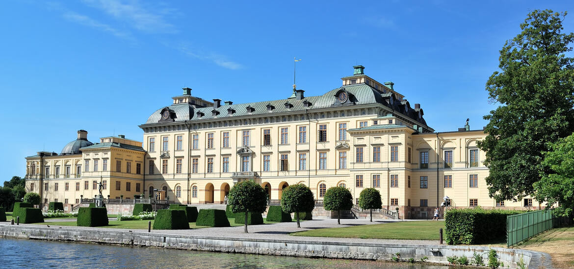 A view of Drottningholm Palace in Stockholm, Sweden, showcasing its symmetrical architecture, lush gardens, and waterside setting 