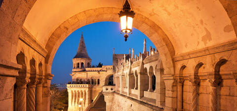 A night view of the illuminated North Gate of Fisherman's Bastion in Budapest, with its arched corridors and a pointed tower