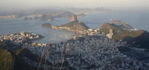 A photo overlooking Rio de Janeiro with buildings in a valley meeting a bay with mountains in the background.
