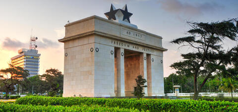 The Independence Arch in Accra, inscribed with Freedom and Justice and topped with two black stars, set against a sunset sky 