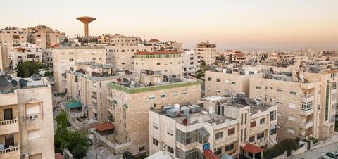 An evening view of the beige stone residential buildings of Amman, Jordan, with a prominent water tower in the background