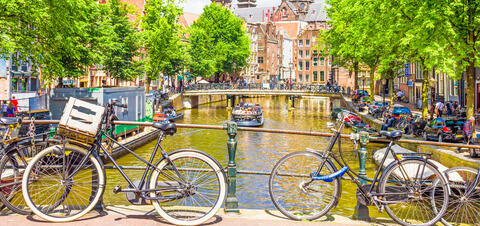 A view of an Amsterdam canal with bicycles parked on a bridge and a boat cruising below, surrounded by traditional Dutch buildings