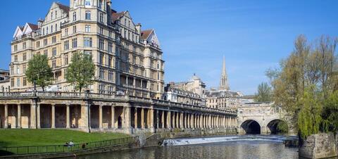 Historic Cityscape along the River Avon in Bath, United Kingdom A view of historic buildings along the River Avon in Bath, Somerset, with classic stone architecture, trees, and a bridge