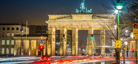 The illuminated Brandenburg Gate in Berlin, Germany, at night with light trails from passing cars in the foreground