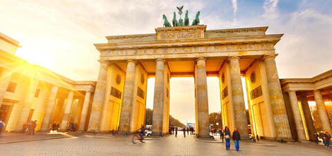 The iconic Brandenburg Gate in Berlin, Germany, glowing in the warm light of sunset with people walking and cycling through its arches