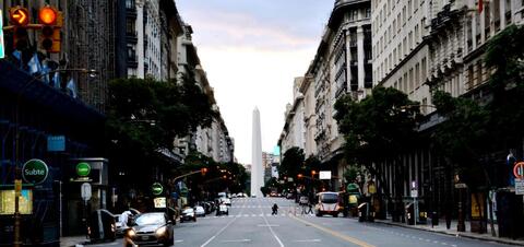 A view down Avenida 9 de Julio in Buenos Aires, Argentina, showing the iconic Obelisk at the far end of the street, flanked by historic buildings and traffic lights