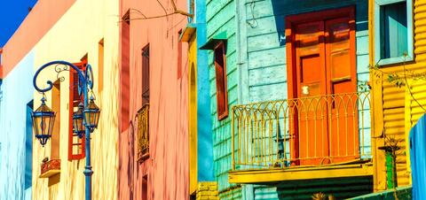 Close-up of vibrant, multi-colored residential buildings in the La Boca neighborhood of Buenos Aires, Argentina, featuring bright blue, yellow, orange, and green walls with decorative balconies and ornate street lamps