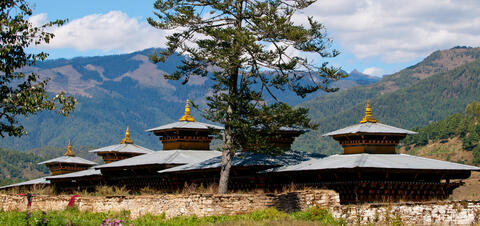 View of a monastery in Jakar, Bhutan, with golden rooftops, surrounded by mountains and trees in the Bumthang valley