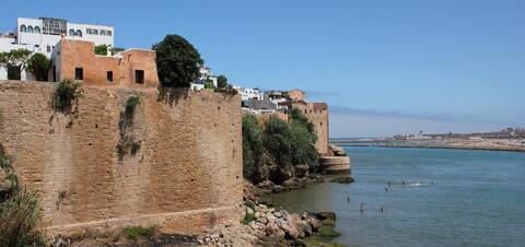 Stone fortress walls and buildings perched on a cliffside overlooking the Bou Regreg River in Rabat, Morocco, with a view of the distant coastline