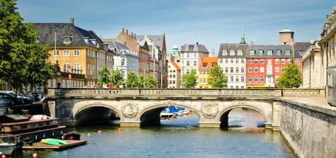 City Center of Copenhagen, Denmark A picturesque view of a historic stone bridge over a canal in Copenhagen, lined with colorful, traditional buildings and trees