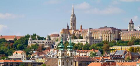  A panoramic view of the Buda side of Budapest featuring the Fisherman's Bastion and Matthias Church, with their distinctive spires and towers, set against a backdrop of historic buildings