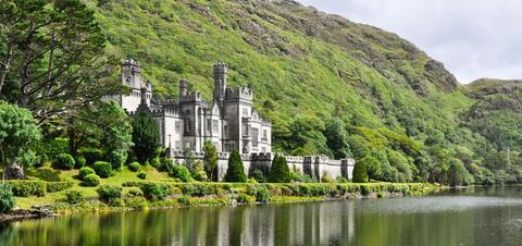 Kylemore Abbey in Connemara, Ireland A scenic view of Kylemore Abbey, a historic castle surrounded by lush greenery, set against the backdrop of the Connemara Mountains and reflected in a lake