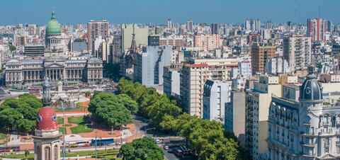 An aerial view of Buenos Aires, Argentina, highlighting the National Congress building surrounded by dense urban development, green parks, and a mix of historical and modern architecture