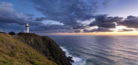 View of the Cape Byron Lighthouse perched on a cliff, overlooking the ocean at sunrise