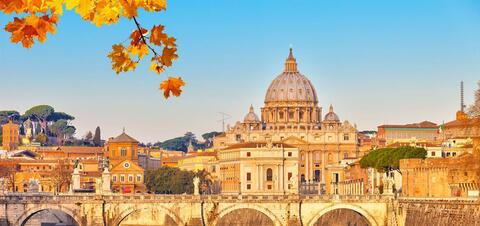 A scenic view of St. Peter's Basilica in Vatican City, with its iconic dome, seen from across the Tiber River 