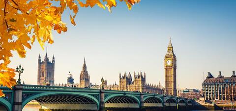 Big Ben and the Houses of Parliament in London, framed by autumn leaves with Westminster Bridge in the foreground