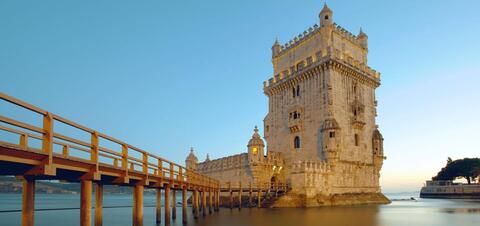 A view of the historic Belem Tower in Lisbon, Portugal, with a wooden bridge leading to it at dusk