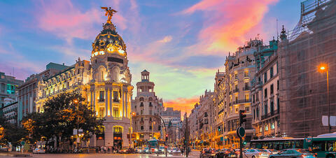 Evening view of Gran Vía in downtown Madrid, with the illuminated Metropolis building and surrounding architecture