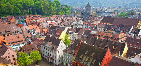 An aerial view of the vibrant red-tiled rooftops of Freiburg, Germany, with the historic clock tower and surrounding greenery in the background