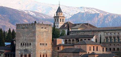 A view of the Alhambra in Granada, Spain, with its historic towers and intricate architecture framed by the snowy Sierra Nevada mountains in the background