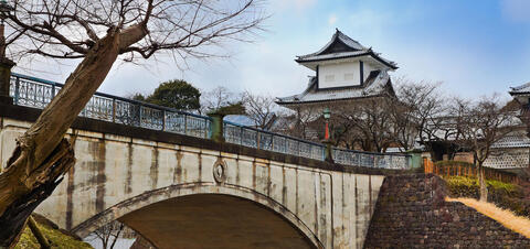 Kanazawa Castle with its traditional Japanese architecture, seen from below a stone bridge, surrounded by bare trees in Ishikawa, Japan