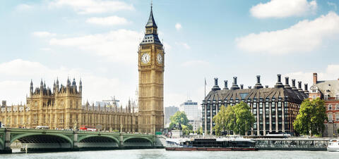 Big Ben and the Houses of Parliament viewed from across the River Thames, with trees and historic buildings under a bright sky