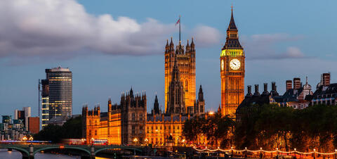 Iconic view of Big Ben and the Houses of Parliament in London at dusk, with the clock tower illuminated and modern city buildings in the background