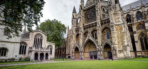 A view of Westminster Abbey in London, featuring its intricate Gothic architecture and large rose window, framed by green trees 