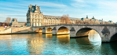 A stone bridge crossing a river with the Louvre Museum in the background