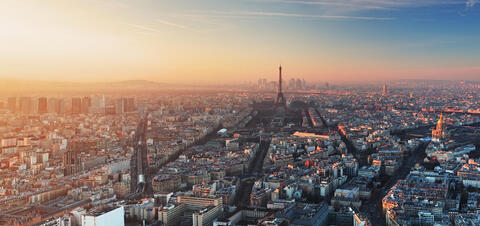 A panoramic view of Paris at sunset, with the Eiffel Tower standing prominently and the city bathed in a warm, golden light