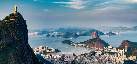 Panoramic view of Rio de Janeiro, featuring the iconic Christ the Redeemer statue on a mountain, with the city, bay, and distant hills in the background