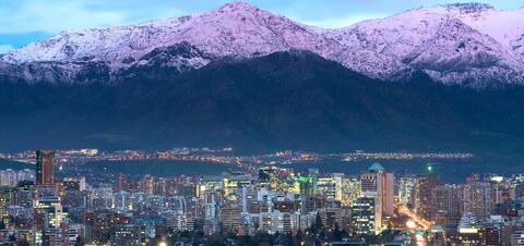 A view of Santiago's city skyline at dusk, with the snow-capped Andes Mountains in the background