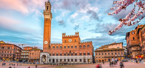 A red brick building with a clock tower overlooking a piazza
