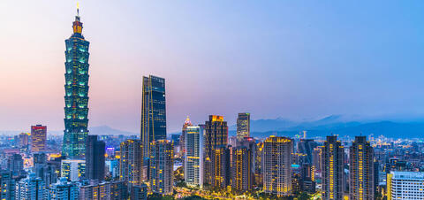 A panoramic view of Taipei's skyline during dusk, featuring the iconic Taipei 101 skyscraper surrounded by high-rise buildings and mountains in the bakground