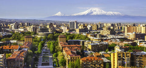 A view of Yerevan, the capital city of Armenia, with its mix of modern and historic architecture, lush green parks, and the iconic snow-capped peaks of Mount Ararat in the background