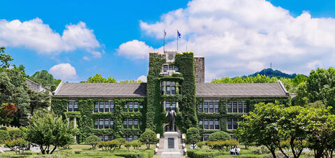 A view of the iconic ivy-covered main building at Yonsei University in Seoul, with a statue in front and surrounded by lush gardens