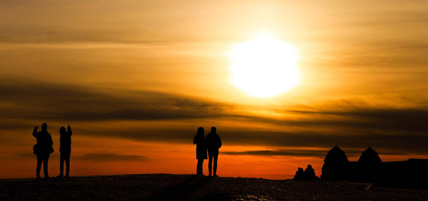 Silhouettes of people are standing and watching the sun set.