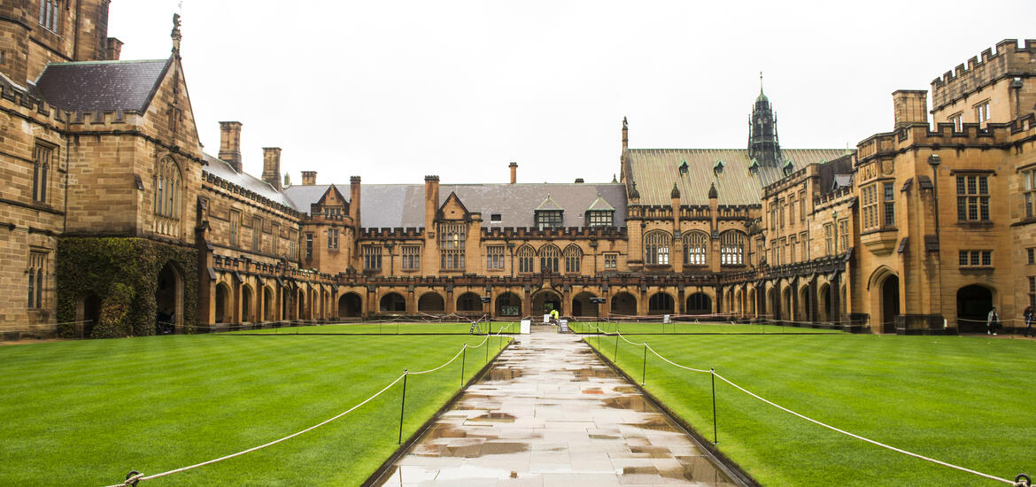 View of the historic Quadrangle building at the University of Sydney, featuring Gothic-style architecture and a green lawn