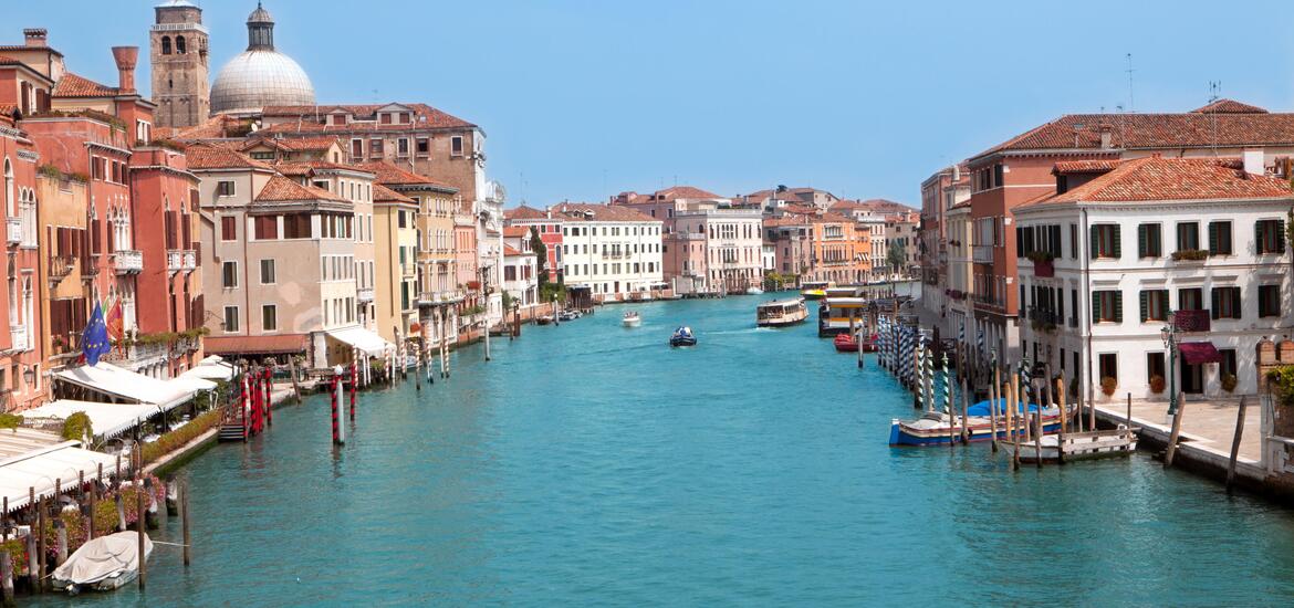 An aerial view of the Grand Canal in Venice, Italy, with boats and water taxis navigating between colorful historic buildings along the water's edge