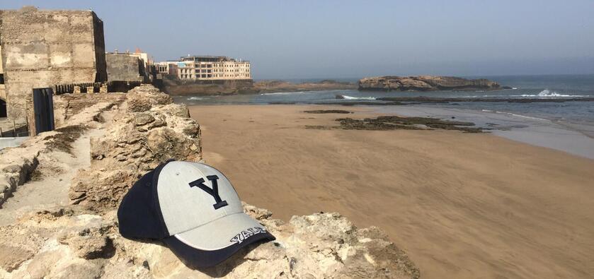 A Yale baseball cap lies on a rock in the foreground with a beach in the background