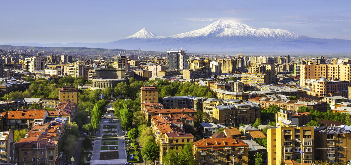A view of Yerevan, the capital city of Armenia, with its mix of modern and historic architecture, lush green parks, and the iconic snow-capped peaks of Mount Ararat in the background