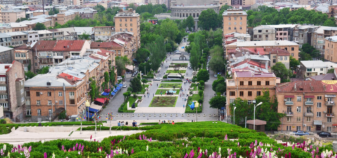 Overhead view of the Yerevan Cascade complex, with its manicured gardens and central walkway, leading down to the surrounding buildings and city center of Yerevan, Armenia